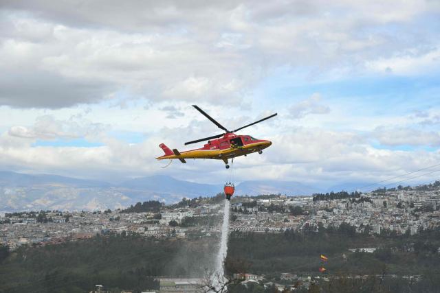 A helicopter providing support to extinguish the fire is seen on the southern side of Casitagua Hill, in northern Quito, on September 18, 2026. Firefighters battled wildfires sweeping through a forest in Ecuador's capital Quito on September 18, with authorities saying they had evacuated dozens of people. (Photo by Rodrigo BUENDIA / AFP)