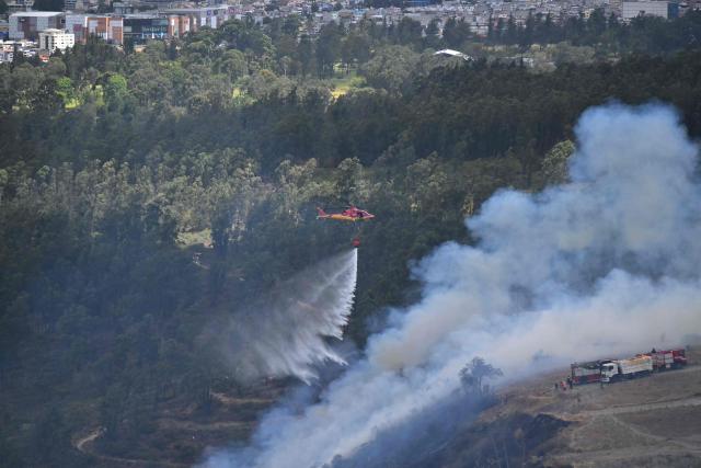 A helicopter providing support to extinguish the fire is seen on the southern side of Casitagua Hill, in northern Quito, on September 18, 2026. Firefighters battled wildfires sweeping through a forest in Ecuador's capital Quito on September 18, with authorities saying they had evacuated dozens of people. (Photo by Rodrigo BUENDIA / AFP)