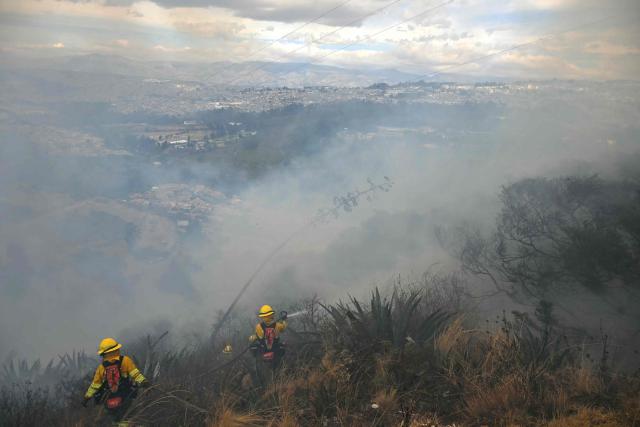 Firefighters work to control a fire on the southern side of Casitagua Hill, in northern Quito on September 18, 2026. Firefighters battled wildfires sweeping through a forest in Ecuador's capital Quito on September 18, with authorities saying they had evacuated dozens of people. (Photo by Rodrigo BUENDIA / AFP)