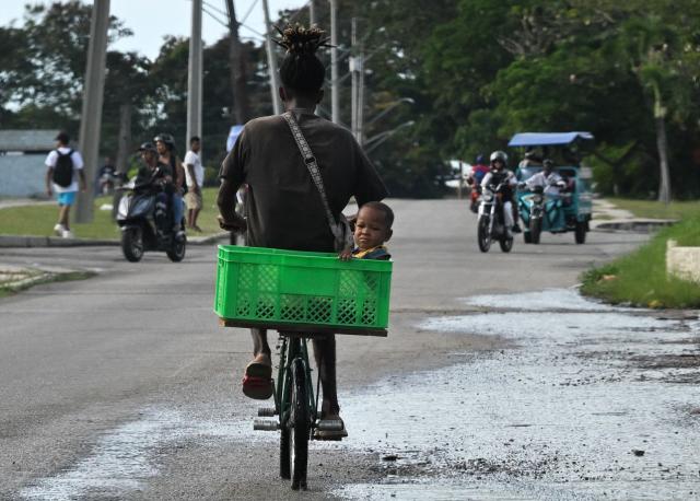A man rides a bicycle with his son during a widespread power outage on September 18, 2026. Cuba was plunged into its seventh massive blackout of the year on September 18, 2026, the energy ministry said, as fuel shortages bite on the US-blockaded island. (Photo by YAMIL LAGE / AFP)
