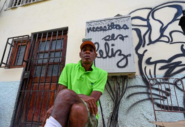 A man sits in front of a sign reading "Necesitas ser feliz" (You need to be happy) during a blackout in Havana on September 18, 2026. Cuba was plunged into its seventh massive blackout of the year on September 18, 2026, the energy ministry said, as fuel shortages bite on the US-blockaded island. (Photo by ADALBERTO ROQUE / AFP)