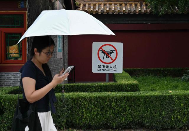 A woman walks past a "No Drone Zone" sign in Beijing on September 19, 2026. New rules in the Chinese capital ban not just the flying of unmanned aerial vehicles but the possession or storage of them, meaning owners have until November 15 to get rid of their drones. (Photo by ADEK BERRY / AFP)