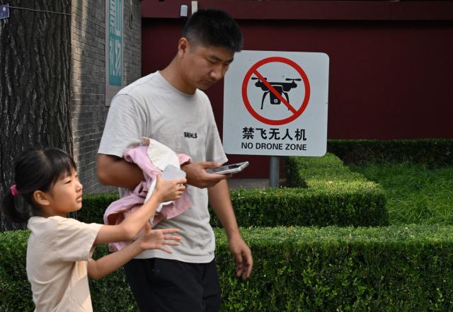 People walk past a "No Drone Zone" sign in Beijing on September 19, 2026. New rules in the Chinese capital ban not just the flying of unmanned aerial vehicles but the possession or storage of them, meaning owners have until November 15 to get rid of their drones. (Photo by ADEK BERRY / AFP)