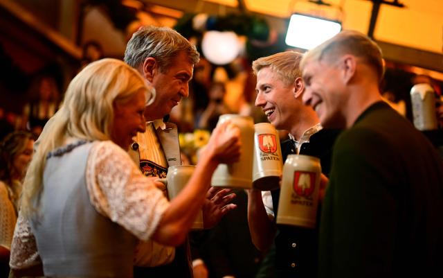 Bavaria's State Premier Markus Soeder (2nd L), his wife Karin Baumueller-Soeder (L), the mayor of Munich Dominik Krause (2nd R) and his partner Sebastian Mueller (R) clink their beer mugs after the first barrel of beer was tapped with the traditional "O´zapft is!" (It's tapped!) to start Munich's annual beer festival, the Oktoberfest, on September 19, 2026 in Munich, southern Germany. The world's biggest beer festival Oktoberfest runs until October 4, 2026. (Photo by Tobias SCHWARZ / AFP)