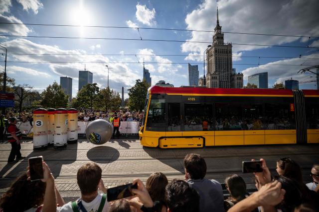 Spectators watch as one of the competitors hit the giant ball during tram bowling chalange during the 12th European Tram Driver Championship in front of the Palace of Culture and Science on Marszalkowska Street in downtown Warsaw, on 19 September 2026. 26 teams – each consisting of a female and a male tram driver, from 25 cities and 24 European countries, plus one guest team from Melbourne, Australia – show off their driving skills in a series of challenging competitions that test their precision, concentration, feel for the vehicle, and control of the tram. (Photo by Wojtek RADWANSKI / AFP)