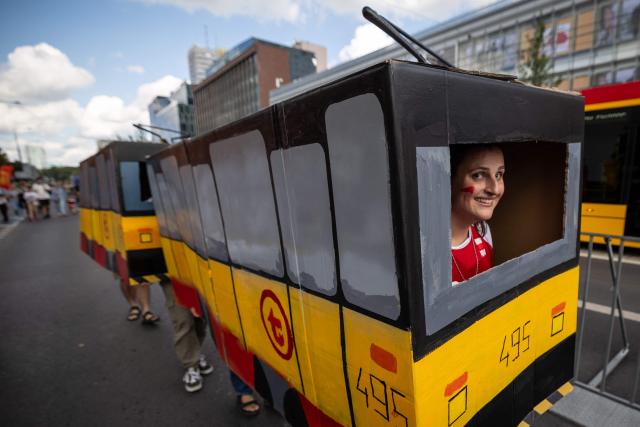 A group of fans dressed as a cardboard mock-up Warsaw tram is entertaining spectators during the 12th European Tram Driver Championship in front of the Palace of Culture and Science on Marszalkowska Street in central Warsaw on 19 September 2026. 26 teams – each consisting of a female and a male tram driver, from 25 cities and 24 European countries, plus one guest team from Melbourne, Australia – show off their driving skills in a series of challenging competitions that test their precision, concentration, feel for the vehicle, and control of the tram. (Photo by Wojtek RADWANSKI / AFP)