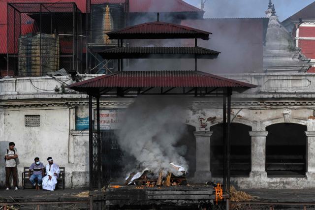 Family members sit beside the burning pyre of a flash flood victim during a funeral ceremony at the Pashupatinath temple in Kathmandu on September 21, 2026. (Photo by Prakash MATHEMA / AFP)