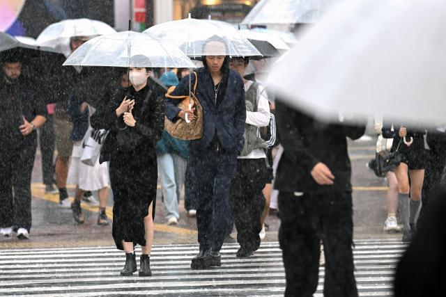 Pedestrians with umbrellas cross a street amid heavy rainfall in Tokyo's Shibuya district on September 21, 2026. (Photo by Rie KIKUCHI / AFP)