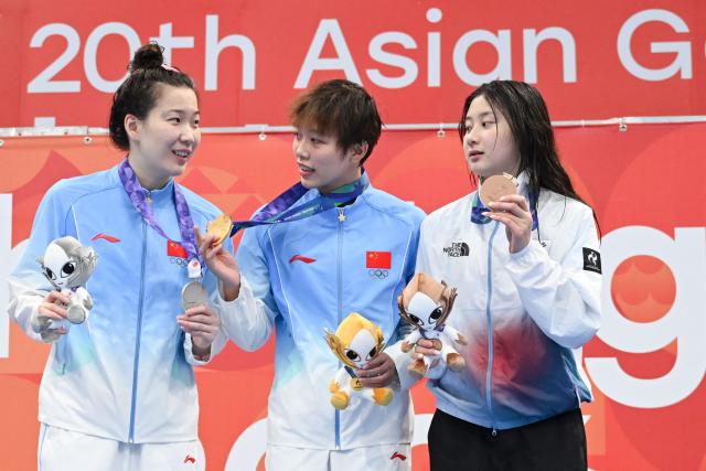 (L-R) Second-placed China's Wang Xueer, winner China's Wan Letian and third-placed South Korea's Kim Seung-won celebrate on the podium during the victory ceremony of the women's 50m backstroke swimming event during the 2026 Asian Games at the Tokyo Aquatics Centre in Tokyo on September 21, 2026. (Photo by ANDREW CABALLERO-REYNOLDS / AFP)