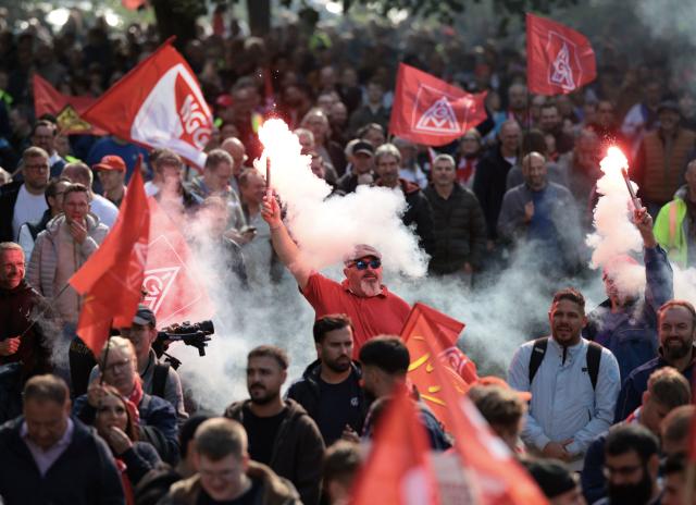 Workers light flares and wave flags of the industrial union IG Metall as they protest against job cuts in front of the commercial cars plant of German car maker Volkswagen (VW) on September 21, 2026 in Hanover, central Germany. The metalworkers' IG Metall union has called for nationwide protests at manufacturers and suppliers in the automotive industry, claiming government and management action to protect jobs and factories as the car industry hits crisis point. (Photo by Ronny HARTMANN / AFP)