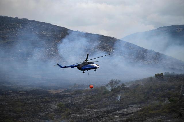A helicopter carrying water to battle a wildfire flies above Ritoque Hill in the municipality of Villa de Leyva, Boyaca department, Colombia, on September 21, 2026. (Photo by Raul ARBOLEDA / AFP)