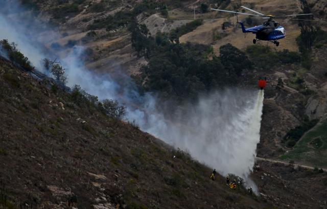 A helicopter drops water on a wildfire burning on Ritoque Hill in the municipality of Villa de Leyva, Boyaca department, Colombia, on September 21, 2026. (Photo by Raul ARBOLEDA / AFP)