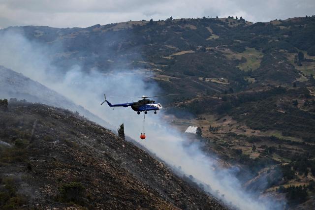 A helicopter carrying water to battle a wildfire flies above Ritoque Hill in the municipality of Villa de Leyva, Boyaca department, Colombia, on September 21, 2026. (Photo by Raul ARBOLEDA / AFP)