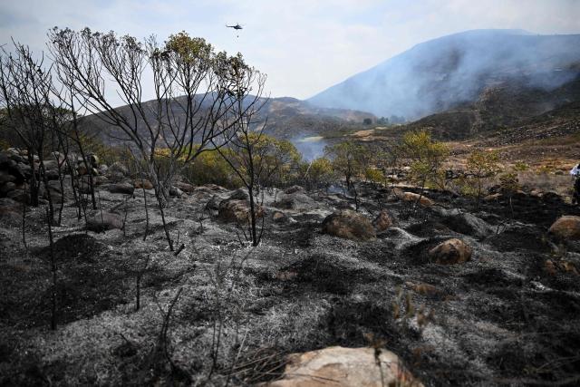 A helicopter carrying water flies above an area charred by a wildfire on Ritoque Hill in the municipality of Villa de Leyva, Boyaca department, Colombia, on September 21, 2026. (Photo by Raul ARBOLEDA / AFP)