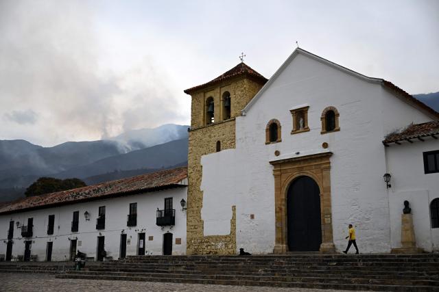 The facade of a church overlooks the main square of Villa de Leyva as smoke rises from a wildfire on Ritoque Hill in Boyaca department, Colombia, on September 21, 2026. (Photo by Raul ARBOLEDA / AFP)
