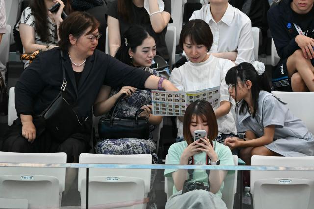 Supporters read a booklet while trying to identify swimmers during a heat of the men's 4 x 100m medley relay swimming event during the 2026 Asian Games at the Tokyo Aquatics Centre in Tokyo on September 22, 2026. (Photo by ANDREW CABALLERO-REYNOLDS / AFP)