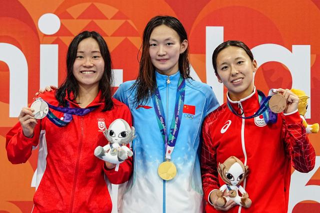 Silver medallist Singapore's Gan Ching Hwee (L), gold medallist China's Li Bingjie (C) abd bronze medallist Japan's Ichika Kajimoto (R) celebrate on the podium during the victory ceremony of the women's 400m freestyle swimming event during the 2026 Asian Games at the Tokyo Aquatics Centre in Tokyo on September 22, 2026. (Photo by Yuichi YAMAZAKI / AFP)