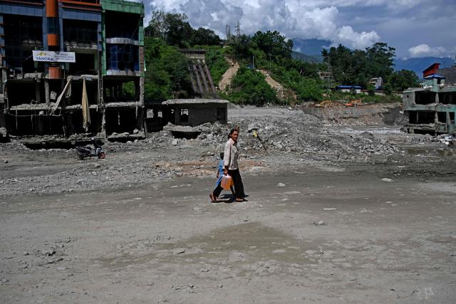 A woman carries petrol whilst she walks past damaged houses in the aftermath of flash floods at Trishuli in Nepal’s Nuwakot district on September 22, 2026. (Photo by PRAKASH MATHEMA / AFP)