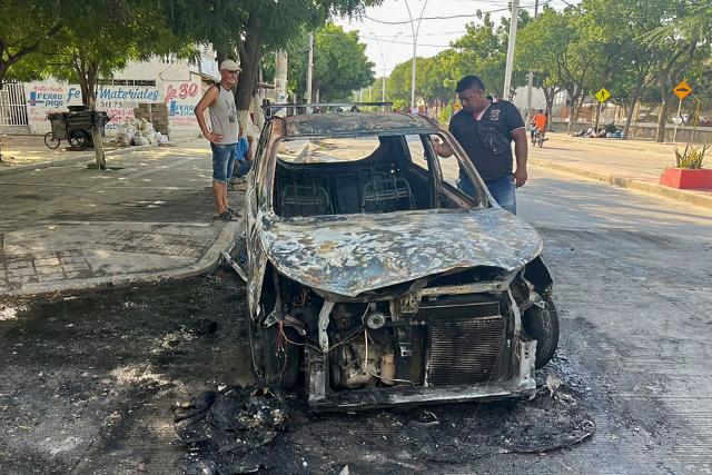 People inspect a burnt car in the wake of a military operation by the Colombian Army against the drug-related armed group Conquering Self Defense Forces of the Sierra Nevada (ACSN) in Santa Marta, Colombia on September 22, 2026. Colombia's President Abelardo de la Espriella sent troops into Santa Marta after an armed group attacked shops and burnt vehicles across the Caribbean city, he announced on September 22, 2026. The chaos followed an earlier announcement by the president that authorities had killed 13 members of the self-styled Conquering Self Defense Forces of the Sierra Nevada (ACSN), an armed group which controls cocaine trafficking routes. (Photo by Idinael Fernandez / AFP)
