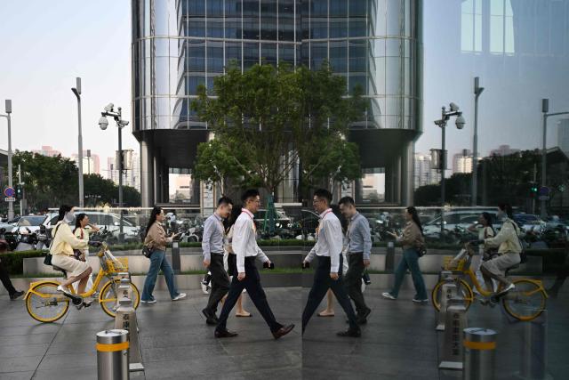 Office workers walk to their buildings in the central business district in Beijing on September 23, 2026. (Photo by GREG BAKER / AFP)