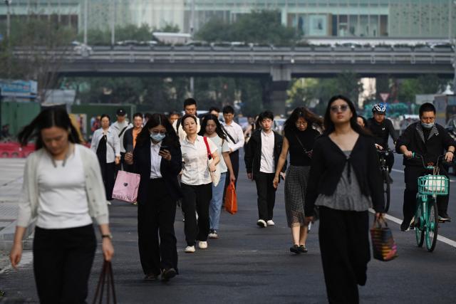 Office workers walk to their buildings in the central business district in Beijing on September 23, 2026. (Photo by GREG BAKER / AFP)