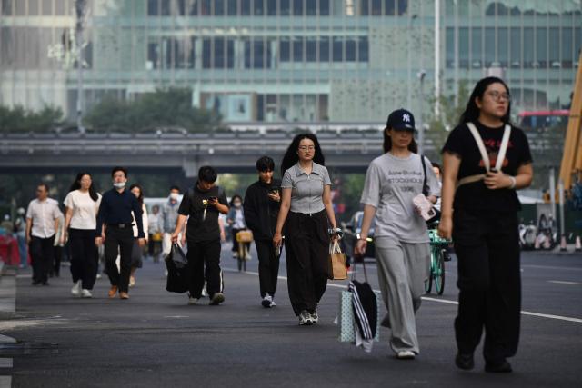 Office workers walk to their buildings in the central business district in Beijing on September 23, 2026. (Photo by GREG BAKER / AFP)