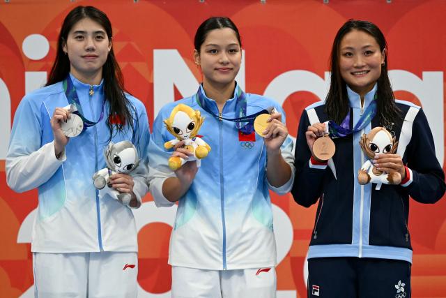 (L-R) Silver medallist China's Yufei Zhang, gold medallist China's Yiting Yu and bronze medallist Hong Kong's Cheuk Tung Natalie Kan celebrate on the podium during the victory ceremony of the women's 100m butterfly swimming event during the 2026 Asian Games at the Tokyo Aquatics Centre in Tokyo on September 23, 2026. (Photo by ANDREW CABALLERO-REYNOLDS / AFP)