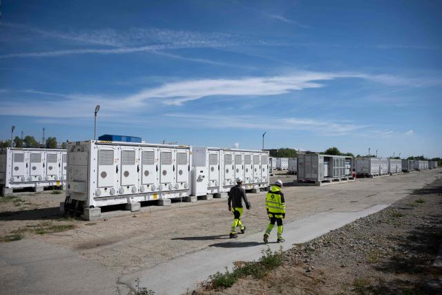 This photograph taken on September 18, 2026, shows workers walking between battery containers in the Contur Global's 500 MWh battery energy storage system near the Maritsa East 3 TPP near Galabovo. As Eastern Europe's power sector has taken a hit from a record drought, Bulgaria has benefitted from a surge in solar-powered battery projects across the country. Around a hundred large battery energy storage system (BESS) sites are now operating, most of them built in the past two years. (Photo by Nikolay DOYCHINOV / AFP)