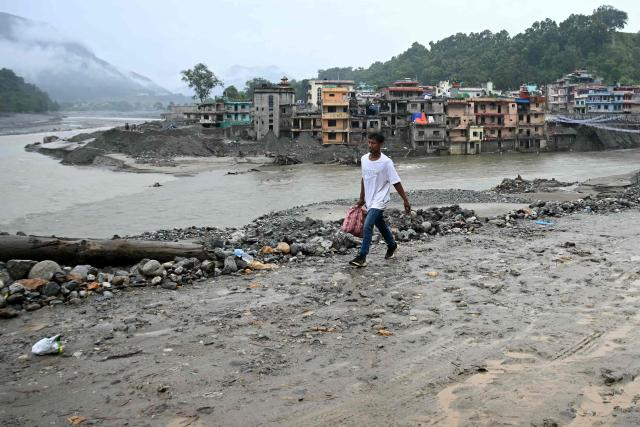 A man walks along a road, damaged during the August 26 flash flood, at Devighat in Nepal's Nuwakot district on September 24, 2026. The catastrophic August 26 flood was triggered by a Himalayan glacial mountain collapse on the China-Nepal border, that scientists have linked to climate change. The tsunmai-like floodwaters tore through mountain districts, destroying roads, bridges and hydropower dams, and killed at least 1,446 people. (Photo by PRAKASH MATHEMA / AFP)
