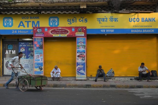 A sweeper pushes a trash trolley past people sitting along a road in Ahmedabad on September 24, 2026. (Photo by Shammi MEHRA / AFP)