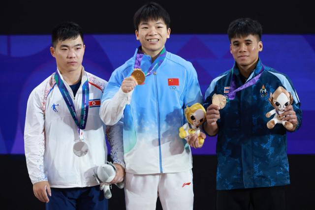 China's Yang Yang (C) celebrates with his gold medal, next to North Korea's Pang Un Chol (L) who won the silver medal and Thailand's Theerapong Silachai (R) who won the bronze medal, after the men's 60kg weightlifting final at the 2026 Asian Games in Nagoya on September 24, 2026. (Photo by DAVID GRAY / AFP)