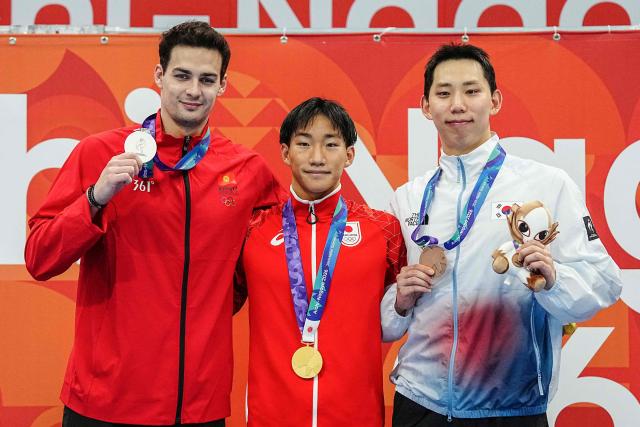 Silver medallist Kyrgyzstan's Denis Petrashov (L) gold medallist and world record holder Japan's Shin Ohashi (C) and South Korea's Cho Sung-jae (R) celebrate on the podium during the victory ceremony of the men's 200m breaststroke swimming event during the 2026 Asian Games at the Tokyo Aquatics Centre in Tokyo on September 24, 2026. (Photo by Yuichi YAMAZAKI / AFP)