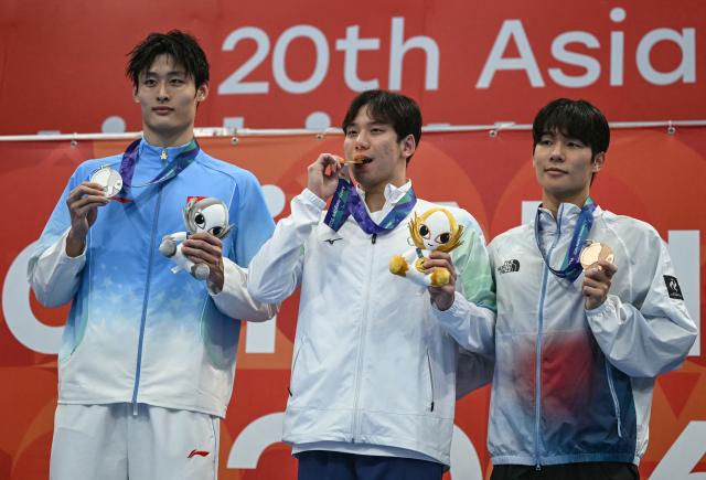 Silver medallist China's Xu Fang (L), gold medallist Taiwan's Wang Kuan-hung (C) and bronze medallist South Korea's Kim Min-seop (R) celebrate on the podium during the victory ceremony of the men's 200m butterfly swimming event during the 2026 Asian Games at the Tokyo Aquatics Centre in Tokyo on September 25, 2026. (Photo by ANDREW CABALLERO-REYNOLDS / AFP)