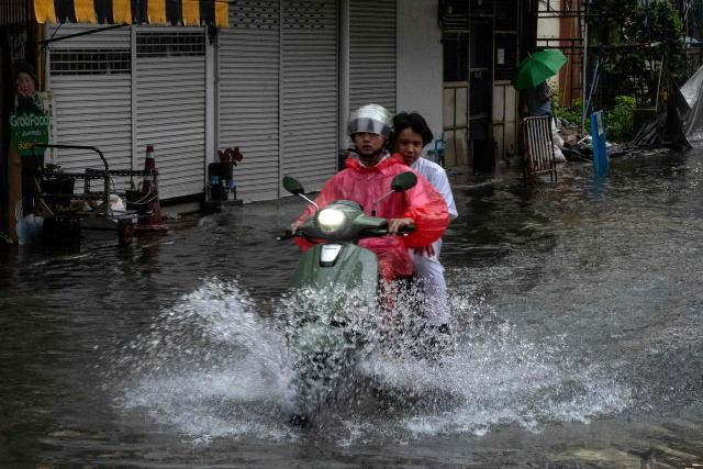 Commuters ride on a scooter through flood waters after heavy rain in Bangkok on September 25, 2026. (Photo by Alex OGLE / AFP)