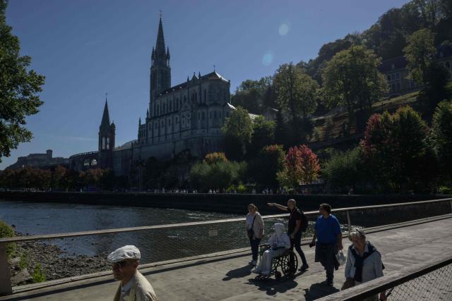 Visitors walk past the Basilica of our Lady of the Rosary in Lourdes, south-western France, a day ahead of the Pope's visit, on September 25, 2026. On the first official papal trip in 18 years to a proudly secular country that has since 1901 separated church and state, Pope Leo will visit Lourdes, a pilgrimage site for Christians worldwide where he will privately meet victims of clerical sex abuse, and Metz, near the German border, where he is to further speak about peace in Europe. (Photo by Ed JONES / AFP)