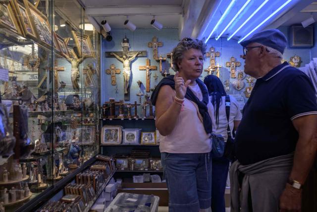Clients stand in a shop with religious souvenirs displayed for sale in Lourdes, south-western France, a day ahead of the Pope's visit, on September 25, 2026. On the first official papal trip in 18 years to a proudly secular country that has since 1901 separated church and state, Pope Leo will visit Lourdes, a pilgrimage site for Christians worldwide where he will privately meet victims of clerical sex abuse, and Metz, near the German border, where he is to further speak about peace in Europe. (Photo by Ed JONES / AFP)