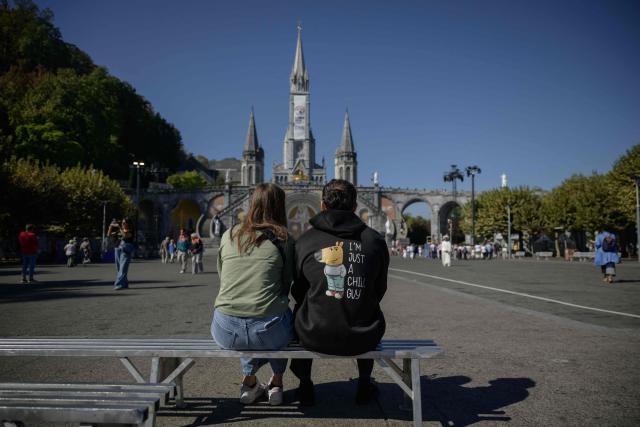 A couple sits before the Basilica of our Lady of the Rosary in Lourdes, south-western France, a day ahead of the Pope's visit, on September 25, 2026. On the first official papal trip in 18 years to a proudly secular country that has since 1901 separated church and state, Pope Leo will visit Lourdes, a pilgrimage site for Christians worldwide where he will privately meet victims of clerical sex abuse, and Metz, near the German border, where he is to further speak about peace in Europe. (Photo by Ed JONES / AFP)