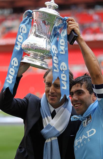 (FILES) Manchester City's manager Roberto Mancini (L) and Argentinian footballer Carlos Tevez celebrate with the FA Cup trophy after beating Stoke 1-0 during the FA Cup final football match between Manchester City and Stoke City at Wembley Stadium in London, on May 14, 2011. Manchester City have been found guilty of all but one of 115 Premier League charges they face for breaching financial regulations, the Athletic reported on Friday, September 25, 2026. (Photo by Adrian DENNIS / AFP)