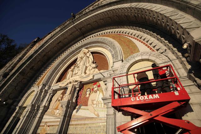(FILES) Workers cover a mosaic made by Marko Rupnik, a Slovenian priest and world-renowned mosaic artist accused of abusing a community of adult religious women in the 1990s, displayed on the Notre-Dame-du-Rosaire Basilica in the Sanctuary of Lourdes in Lourdes, south-western France on March 31, 2025. When he arrives in Lourdes on September 26, 2026, Leo XIV will not see Marko Rupnik’s mosaics, which are everywhere on the basilica’s facade: the monumental work by the Slovenian priest, who has been accused of sexual assault, will have been completely covered up to protect the victims. (Photo by Valentine CHAPUIS / AFP)