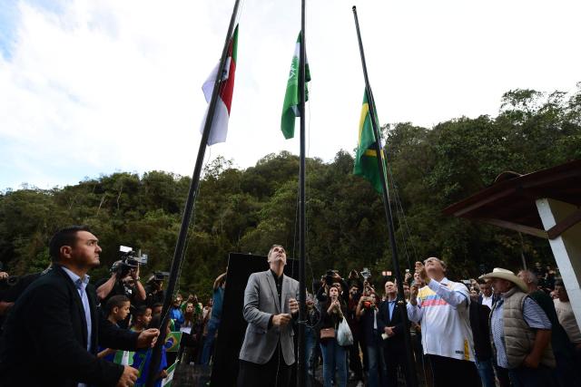 Sergio Escobar Solorzano (R), Brazil's consul in Colombia, raises the Brazilian flag at the memorial of the Chapecoense plane crash ahead of the 10th anniversary of the accident on Cerro Gordo mountain, near La Union, Antioquia department, Colombia on September 25, 2026. On November 28, 2016 the plane flying Chapecoense to Medellin to take on Atletico Nacional in the Copa Sudamericana finals -the biggest and most unexpected game in the Brazilian team's history- ran out of fuel and went down in the mountains near its destination, killing 71 of the 77 aboard, including 19 players. (Photo by Jaime SALDARRIAGA / AFP)