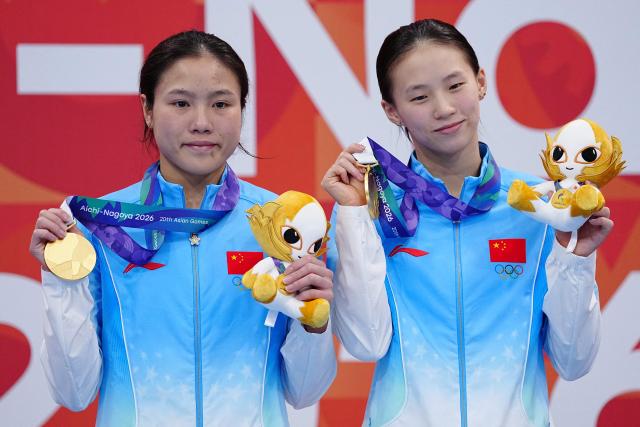 China's Chen Yuxi and Lu Wei pose with their gold medals on the podium during the victory ceremony for the women's synchronised 10m platform final diving event during the 2026 Asian Games at the Tokyo Aquatics Centre in Tokyo on September 26, 2026. (Photo by Yuichi YAMAZAKI / AFP)