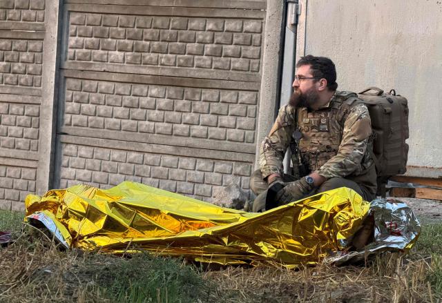 A member of the Ukrainian military sits next to the body of a victim covered by an emergency blanket following an air attack in Zaporizhzhia on September 26, 2026, amid the Russian invasion of Ukraine. (Photo by Darya NAZAROVA / AFP)