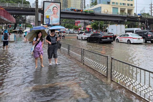 Women hold umbrellas to shield from the rain as they walk through floodwaters in Bangkok on September 26, 2026. Bangkok authorities declared a flood disaster across the Thai capital on September 26 after almost 48 hours of heavy rain left canals full, roads submerged and residents wading through deep water. (Photo by Sara HUSSEIN / AFP)