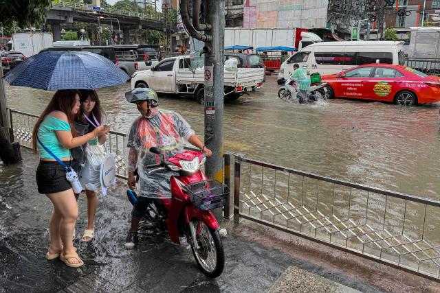 Women taking shelter from the rain under an umbrella ask for directions from a motorcycle taxi rider amid floodwaters in Bangkok on September 26, 2026. Bangkok authorities declared a flood disaster across the Thai capital on September 26 after almost 48 hours of heavy rain left canals full, roads submerged and residents wading through deep water. (Photo by Sara HUSSEIN / AFP)