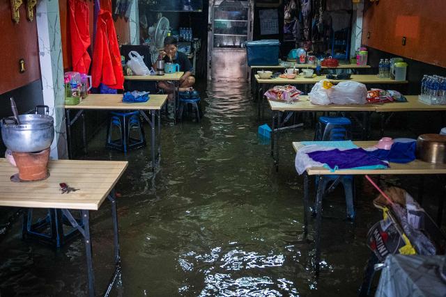A man eats foot in a restaurant submerged in flood waters after heavy rain in Bangkok on September 26, 2026. Bangkok authorities declared a flood disaster across the Thai capital on September 26 after almost 48 hours of heavy rain left canals full, roads submerged and residents knee-deep in water. (Photo by Arnun Chonmahatrakool / THAI NEWS PIX / AFP)