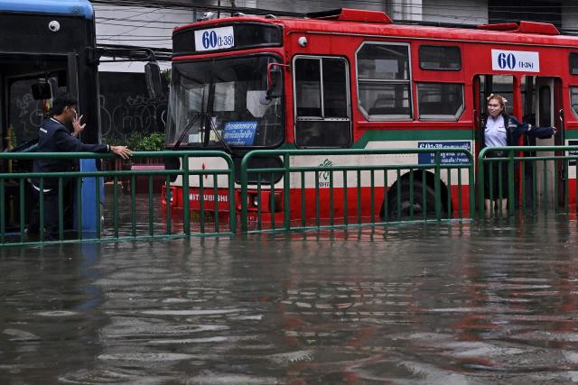 TOPSHOT - Bus conductors chat across stalled public buses along a flooded Petchaburi road in Bangkok on September 26, 2026. Bangkok authorities declared a flood disaster across the Thai capital after almost 48 hours of heavy rain left canals full, roads submerged and residents wading through deep water. (Photo by Lillian SUWANRUMPHA / AFP)