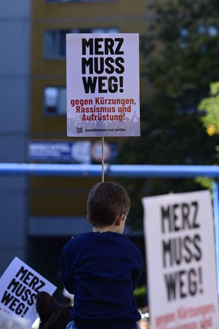 A young boy on someone's shoulders displays a placard reading "Merz must go" during a protest against health insurance and pension reforms organised by the German Trade Union Confederation (DGB), attended by leaders of The Left party (Die Linke), in Berlin on September 26, 2026. (Photo by John MACDOUGALL / AFP)