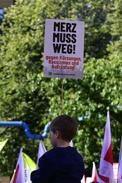 A young boy on someone's shoulders displays a placard reading "Merz must go" during a protest against health insurance and pension reforms organised by the German Trade Union Confederation (DGB), attended by leaders of The Left party (Die Linke), in Berlin on September 26, 2026. (Photo by John MACDOUGALL / AFP)
