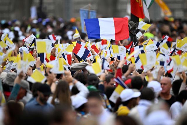 People wave Vatican and French flags as they gather on the Champs-Elysees avenue ahead of the Pope's solemn outdoor mass at Place de la Concorde in central Paris, on September 26, 2026 on the second day of his visit to France. (Photo by JULIEN DE ROSA / AFP)