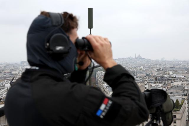 A member of French Police Brigade d'Intervention (BI) of Paris unit watch through binoculars ontop of the Arc de Triomphe monument as the crowd gather on the Champs-Elysees avenue to attend the Pope's solemn outdoor mass at Place de la Concorde in central Paris, on September 26, 2026 on the second day of his visit to France. (Photo by Sameer AL-DOUMY / AFP)
